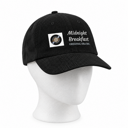 A black baseball cap displayed on a white mannequin head against a plain white background. The cap features a white embroidered logo that reads 'Midnight Breakfast ORIGINAL SEA INC.