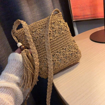 Handmade crochet bag with tassel held by a person, placed on a wooden surface.